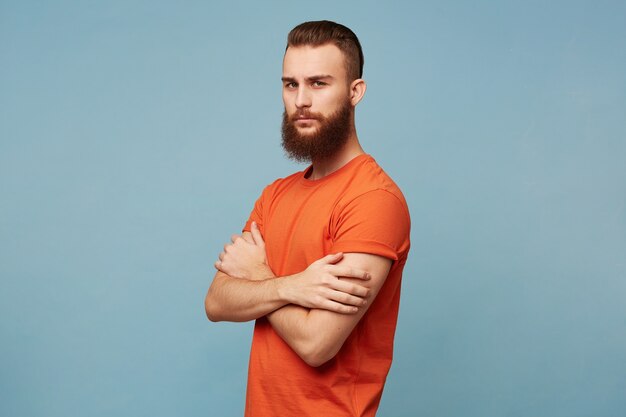 Foto grátis homem forte e sério homem moderno com barba e um corte de cabelo da moda vestindo uma camiseta vermelha fica com os braços cruzados