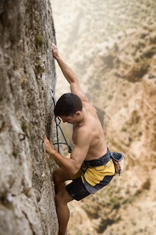 Homem forte escalando montanha com equipamento de segurança