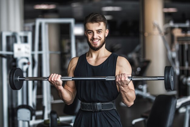 Homem forte, fisiculturista em roupas esportivas com halteres em uma academia, se exercitando com uma barra