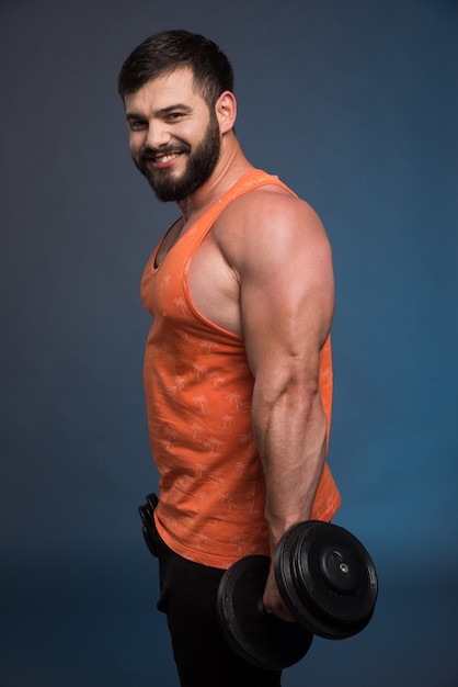 Foto grátis homem forte segurando um haltere na parede azul escura.