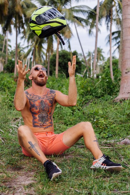 Homem forte tatuado em campo de selva tropical com moto vermelha