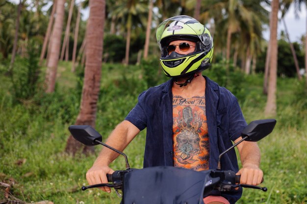 Homem forte tatuado em campo de selva tropical com moto vermelha