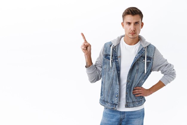 Homem gay bonito de aparência séria com cabelo loiro apontando o dedo para cima e olhando para a câmera focada insiste em clicar no link sugerir produto mostrando caminho para o fundo branco do banner da empresa