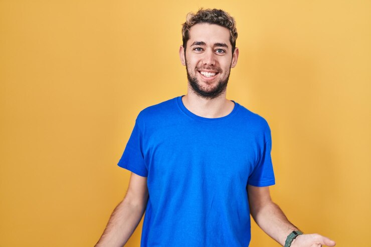 Foto grátis homem hispânico com barba em pé sobre fundo amarelo sorrindo alegre de braços abertos como saudações positivas e confiantes de boas-vindas amigáveis