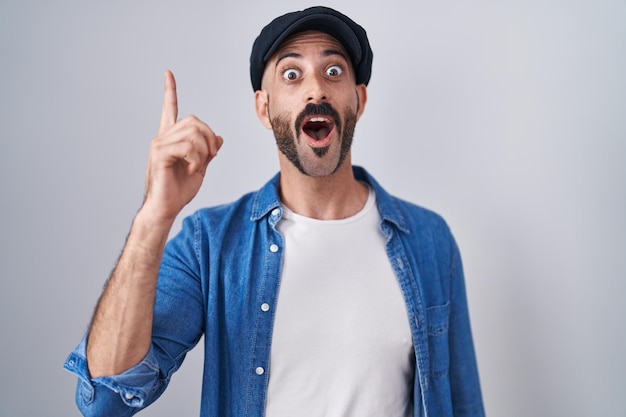 Homem hispânico com barba em pé sobre fundo isolado, apontando o dedo para cima com a ideia de sucesso. saiu e feliz. número um.