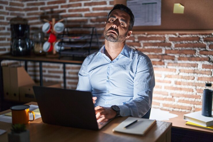 Foto grátis homem hispânico com barba trabalhando no escritório à noite parecendo sonolento e cansado exausto por fadiga e olhos preguiçosos de ressaca pela manhã