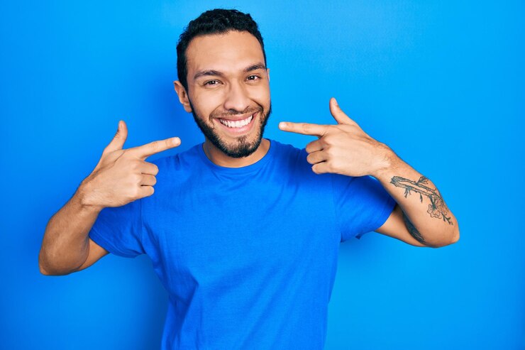 Foto grátis homem hispânico com barba vestindo camiseta azul casual sorrindo alegre mostrando e apontando com os dedos, dentes e boca conceito de saúde bucal
