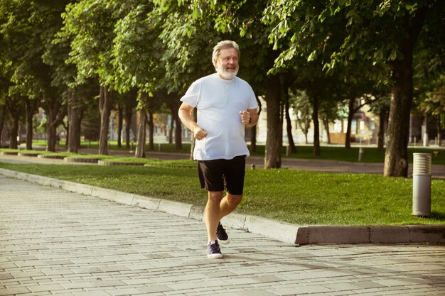 Homem idoso como corredor com braçadeira ou rastreador de fitness nas ruas da cidade