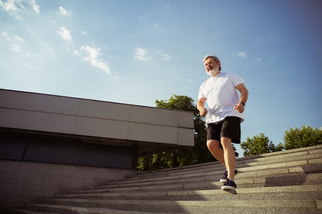 Homem idoso como corredor com braçadeira ou rastreador de fitness nas ruas da cidade