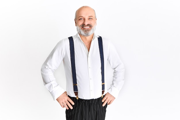 Foto grátis homem idoso emocional feliz com barba grisalha e cabeça careca regozijando-se, segurando as mãos na cintura, sorrindo alegremente, posando contra um fundo branco com espaço de cópia para o seu texto