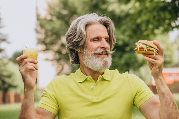 Homem idoso escolhendo entre hambúrguer e maçã