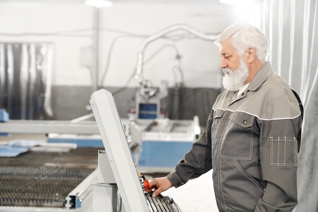 Homem idoso que trabalha com a máquina de corte a laser na fábrica.