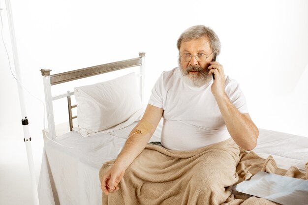 Homem idoso se recuperando em uma cama de hospital, isolada na parede branca. Cuidando. Conceito de saúde e medicina. Copyspace.