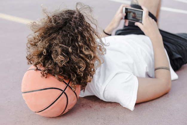 Homem, inclinar-se, seu, encabece basquetebol, usando, telefone móvel