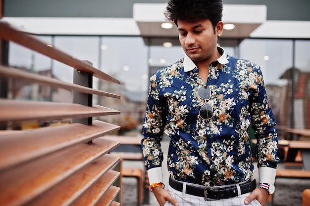 Homem indiano elegante atraente e bonito veste camisa segurando o celular e de pé no terraço do moderno café lounge em seu intervalo de trabalho