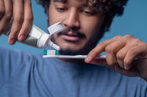 Foto grátis homem indiano focado espremendo a pasta de dente de um tubo de plástico aberto em sua escova de dente