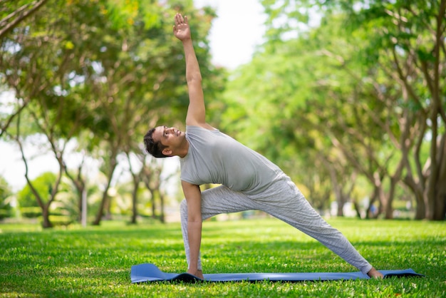 Homem indiano inspirado que faz asanas da ioga no parque da cidade. Cidadão jovem, exercitando fora