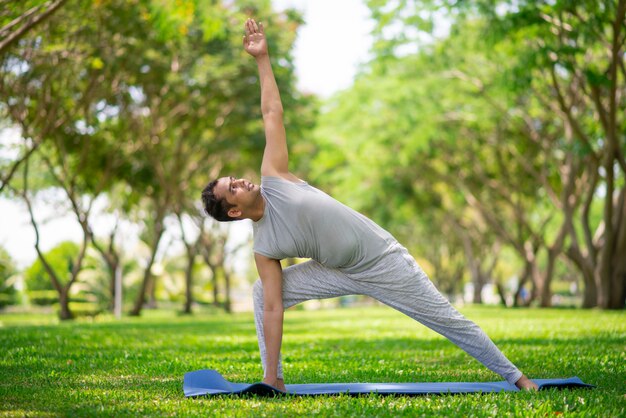 Homem indiano inspirado que faz asanas da ioga no parque da cidade. Cidadão jovem, exercitando fora