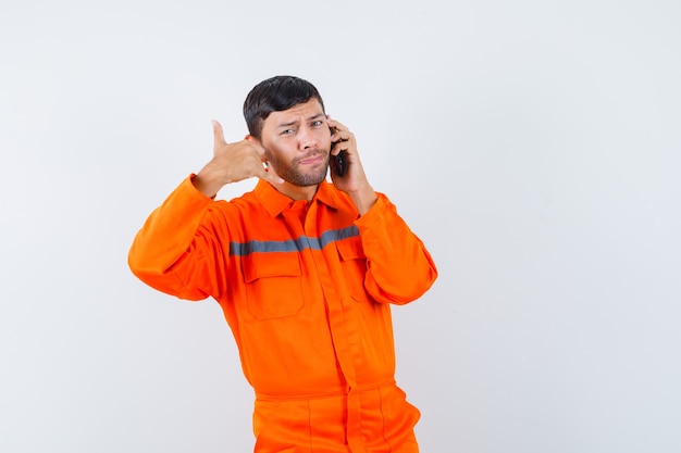 Homem industrial falando no celular com gesto de telefone em vista frontal uniforme.