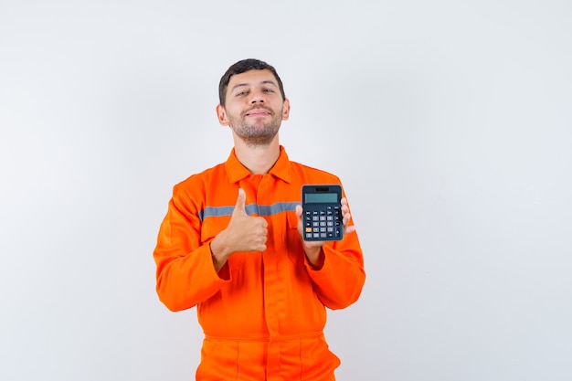 Homem industrial segurando calculadora, aparecendo o polegar de uniforme e parecendo alegre. vista frontal.