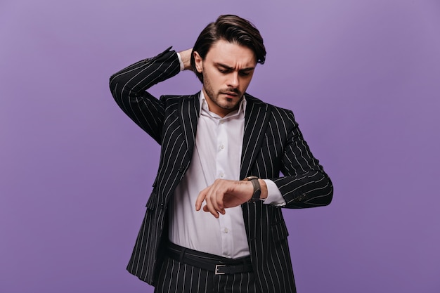 Foto grátis homem inteligente e atraente com cabelo castanho, camisa branca e terno listrado da moda, olhando para o relógio na mão