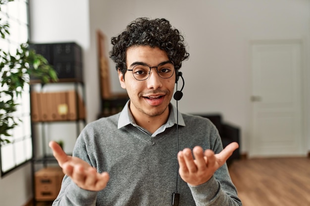 Foto grátis homem jovem agente de call center hispânico sorrindo feliz trabalhando no escritório