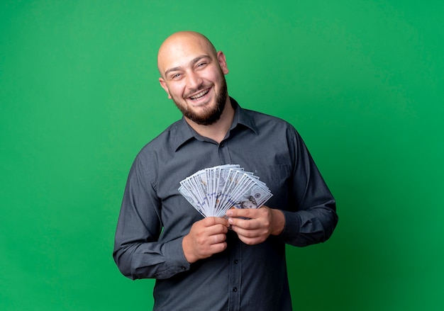 Homem jovem alegre e careca de call center segurando dinheiro isolado no verde
