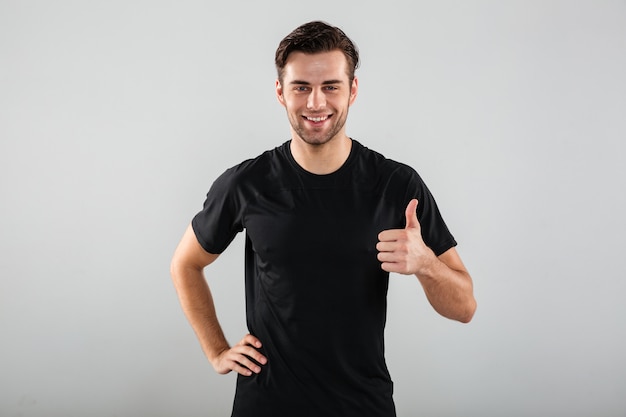 Homem jovem alegre esportes posando mostrando os polegares para cima gesto.