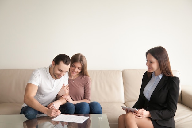 Homem jovem, assinando, papeis, sentando, perto, esposa, e, corretor de imóveis