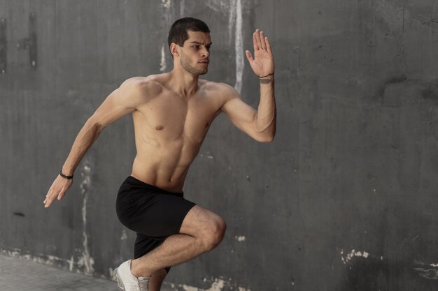 Homem jovem atleta, torso nu, correndo contra uma parede cinza