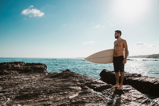 Homem jovem, com, tábua surf, ligado, pedra, perto, mar