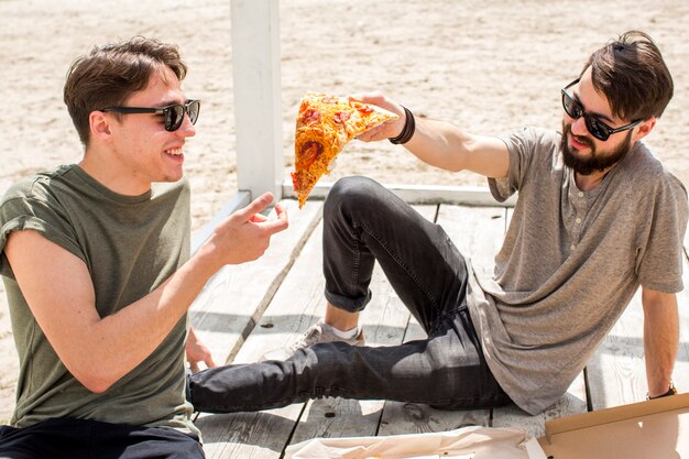 Foto grátis homem jovem, compartilhar, pedaço pizza, com, amigo, ligado, praia
