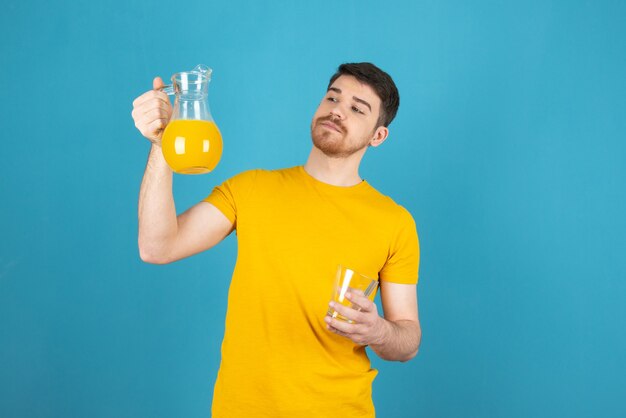 Homem jovem confiante segurando a garrafa cheia de suco de laranja fresco e olhando para ela.