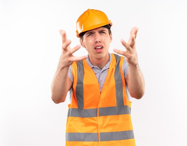 Homem jovem construtor confuso, de uniforme, segurando as mãos isoladas na parede branca