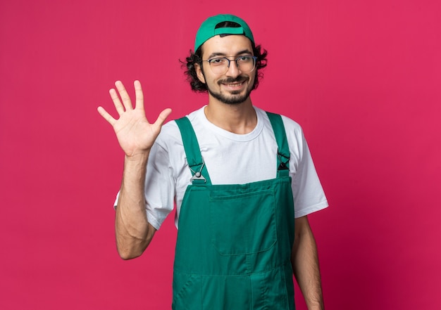 Homem jovem construtor sorridente usando uniforme com boné mostrando gesto de pare