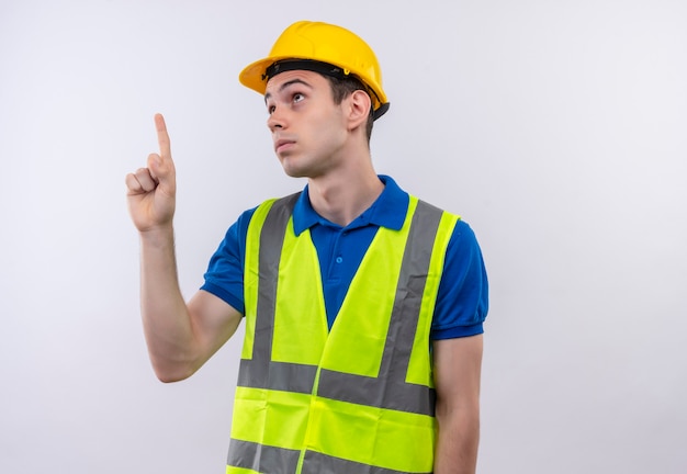 Foto grátis homem jovem construtor usando uniforme de construção e capacete de segurança aponta confuso
