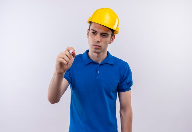 Homem jovem construtor usando uniforme de construção e capacete de segurança, escrevendo com uma caneta