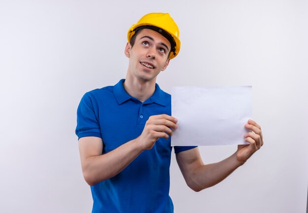 Homem jovem construtor usando uniforme de construção e capacete de segurança segura um papel