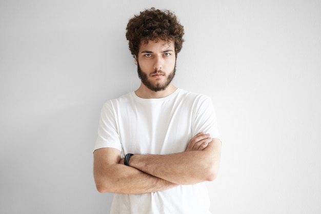 Foto grátis homem jovem e bonito isolado relutante com penteado estiloso e barba por fazer expressando desaprovação ou desrespeito, com olhar sombrio, mantendo os braços cruzados sobre o peito