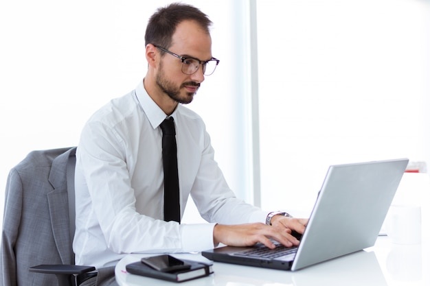 Homem jovem e bonito que trabalha com laptop no escritório.