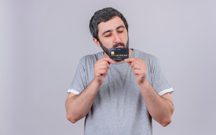Foto grátis homem jovem e bonito satisfeito segurando e beijando um cartão de crédito com os olhos fechados, isolado na parede branca