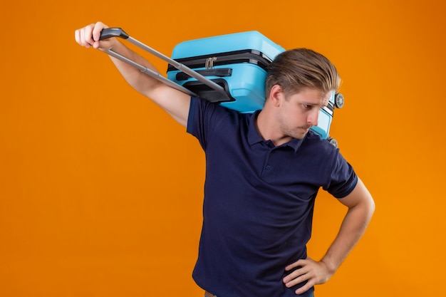 Foto grátis homem jovem e bonito viajante parado com uma mala, parecendo cansado e entediado com o fundo laranja