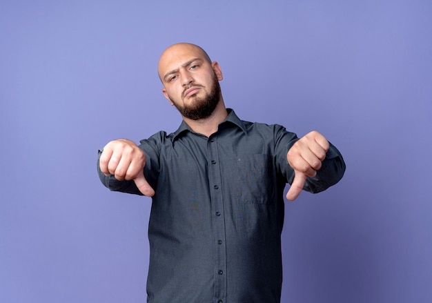 Foto grátis homem jovem e careca irritado com os polegares para baixo, isolado em um fundo roxo com espaço de cópia