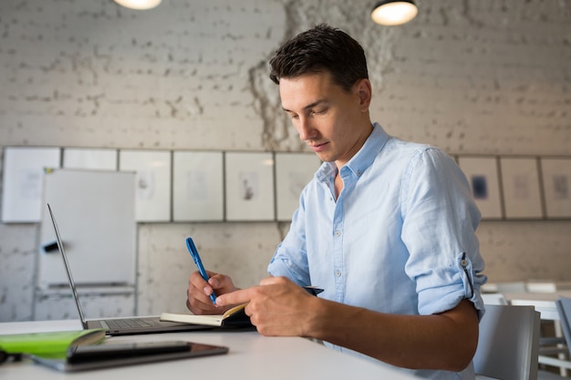 Homem jovem e moderno bonito pensando, escrevendo notas no caderno