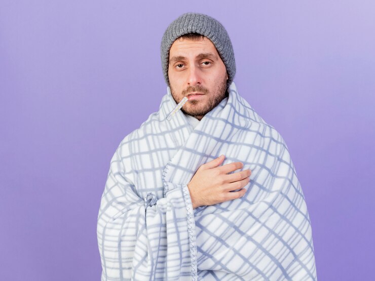 Foto grátis homem jovem e triste com chapéu de inverno e lenço enrolado em uma manta segurando o termômetro na boca, isolado no fundo roxo