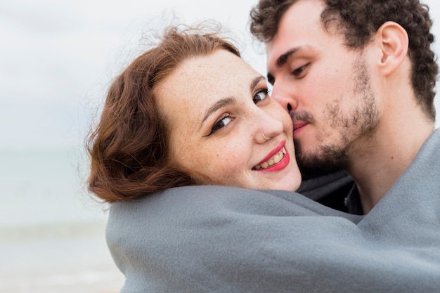 Foto grátis homem jovem, em, cobertor, beijando, mulher, ligado, bochecha