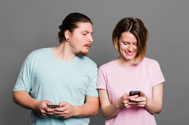 Homem jovem, espiando, e, espiando, em, smartphone, de, dela, namorada, usando, telefone móvel