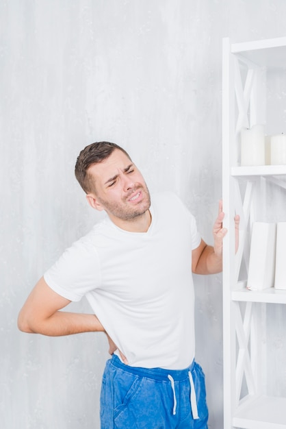 Foto grátis homem jovem, ficar, contra, parede concreta, tocar, seu, costas careta, rosto, com, dor