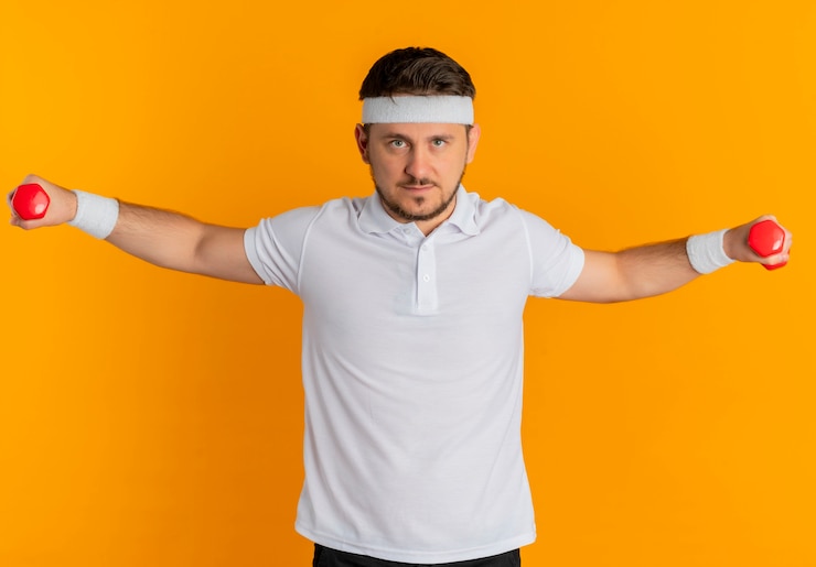 Foto grátis homem jovem fitness com camisa branca e faixa na cabeça, malhando com halteres, parecendo confiante em pé sobre a parede laranja