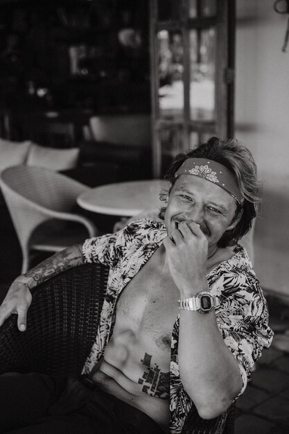 Homem jovem hippie bonito em uma bandana vermelha, com um torso nu em um café em Bali. Homem feliz sorrindo